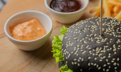 Black burger on a wooden background with potatoes and sauce