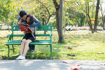 Couple in park sitting on a bench. Talking to each other in romantic and intimate mood. Chinese people.