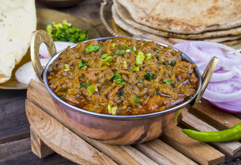 Indian Cuisine Sev Tamatar Also Called Sev Tamaeta or Sev Tameta is Served With Chapati, Papad, Onion or Raita. It is Made With Tomato And Onion Gravy With a Twist of Spicy Sev on Wooden Table