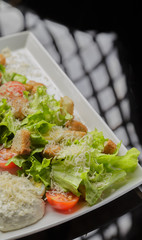 Caesar salad on a white plate and a glass background