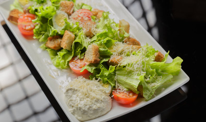 Caesar salad on a white plate and a glass background