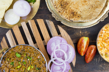 Indian Cuisine Sev Tamatar Also Called Sev Tamaeta or Sev Tameta is Served With Chapati, Papad, Onion or Raita. It is Made With Tomato And Onion Gravy With a Twist of Spicy Sev on Wooden Table