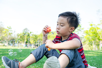 Young boy blowing bubble in park. Chinese boy enjoying playing with his bubble mixture in park.