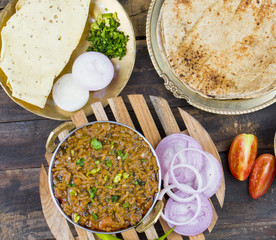 Indian Cuisine Sev Tamatar Also Called Sev Tamaeta or Sev Tameta is Served With Chapati, Papad, Onion or Raita. It is Made With Tomato And Onion Gravy With a Twist of Spicy Sev on Wooden Table