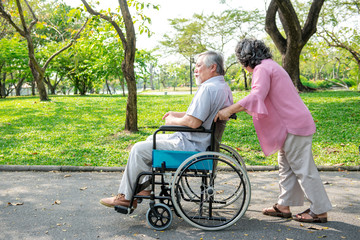 Senior couple in park and in wheelchair. Chinese old couple in park, relaxing, smiling. Man on wheelchair with his wife. Copy space.
