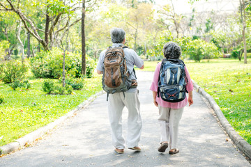Senior couple in park walking with backpack. Chinese old couple in park, relaxing, smiling.