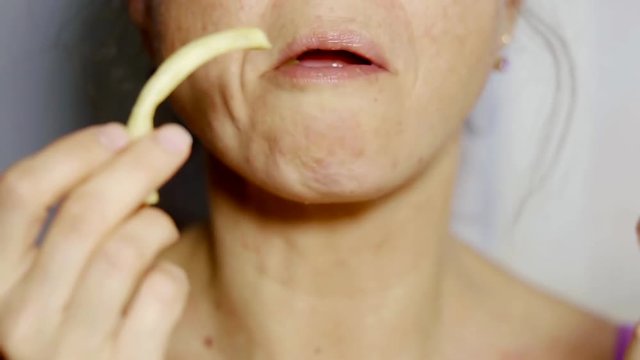 close up shot of the woman's mouth, the lady takes a bite of fried french fries and with pleasure eats fast food