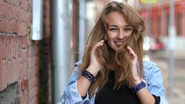 Portrait of beautiful caucasian blonde laughing girl on the street, adjusting hair 