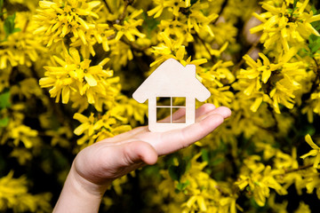 The girl holds the house symbol against the background of blossoming forsythia