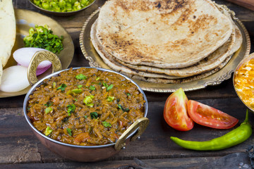 Indian Cuisine Sev Tamatar Also Called Sev Tamaeta or Sev Tameta is Served With Chapati, Papad, Onion or Raita. It is Made With Tomato And Onion Gravy With a Twist of Spicy Sev on Wooden Table