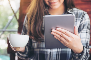 Closeup image of a woman holding and using tablet pc while drinking coffee in cafe