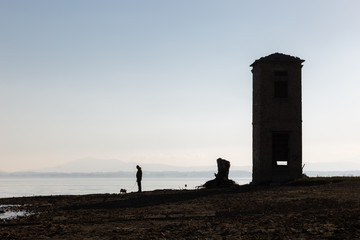 A man walking a dog on a lake shore, beneath a big, empty sky, a