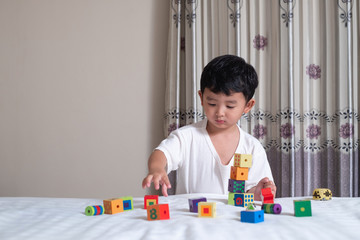 3 years old little cute Asian boy play toy or square block puzzle at home on the bed, kid lying learn by playing block shape or pieces, education and healthy concept idea.