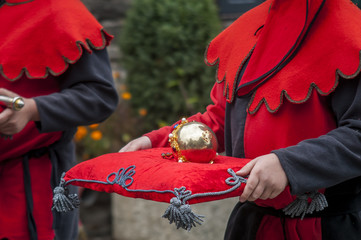 Man in medieval costume holds in his hands red velvet pillow with golden scepter.