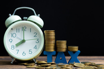 Time to pay TAX concept. TAX alphabet with stack of coin and vintage alarm clock on wooden working table in dark background, business and financial concept.