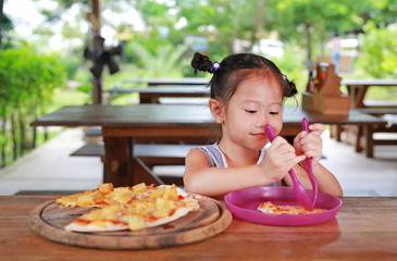 Happy little Asian child eating pizza on the table.