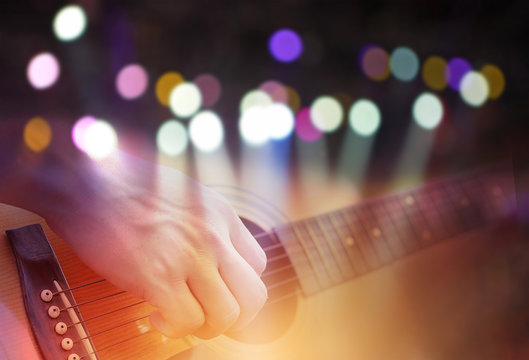 Double exposure of Colored bokeh with concert light image and male hand playing on acoustic guitar.