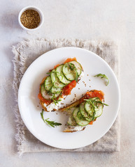 Salmon, cucumber and cream cheese rye sandwich on the wooden background, top view. Delicious snack or appetizer for wine.