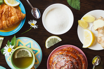 Cup of herbal tea with lemon and mint leaves, ginger root and croissant