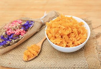 Spiral Macaroni in white bowl on sack against wood background.