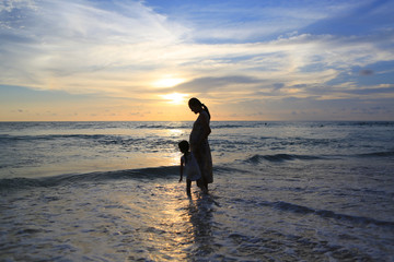 Obraz premium Silhouette Pregnant mother and daughter relaxing on the beach at sunset.