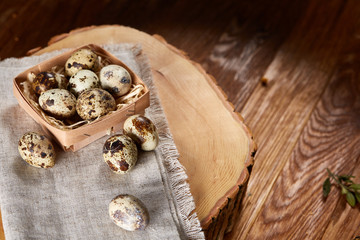 Obraz na płótnie Canvas Composition of eggs quail box, eggs on a homespun napkin on a log over wooden background, top view