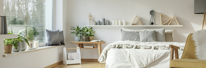 Real photo of a spacious bedroom interior with gray cushions on white bed next to a wooden bedside...