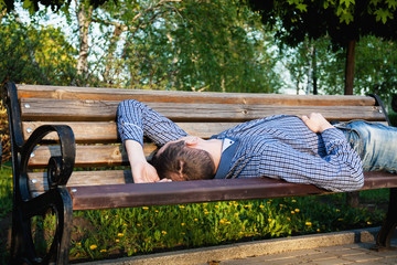 An young man is lying on a bench in the park.