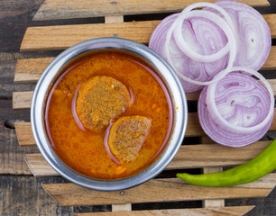 Indian Traditional Cuisine Gatta Curry Also Called Gatte ki Sabji or Besan Gatta is a Rajasthan Famous Food Served with Chapati, Onion, Raita or Papad on Wooden Background