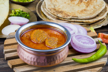 Indian Traditional Cuisine Gatta Curry Also Called Gatte ki Sabji or Besan Gatta is a Rajasthan Famous Food Served with Chapati, Onion, Raita or Papad on Wooden Background