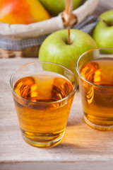 Apple juice in glasses and apples in a wicker basket on wooden table 