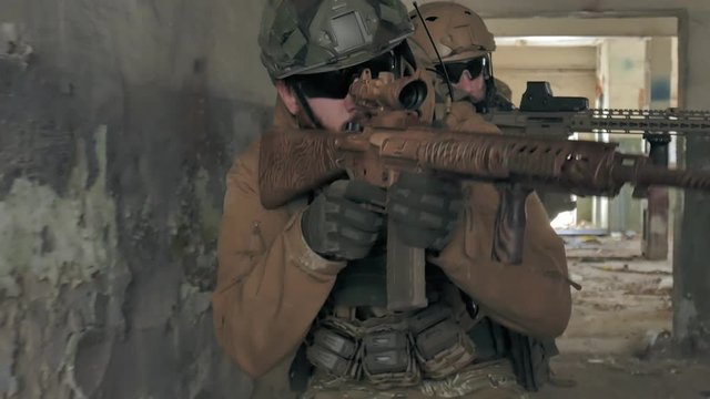 Soldiers in camouflage with combat weapons sneak along the corridors of the old building, the military concept