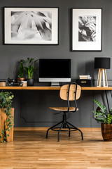 Real photo of a dark, wooden home office interior with empty computer monitor o the desk standing against black wall with molding