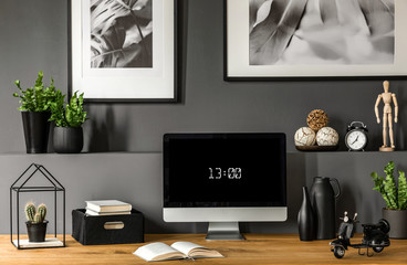 Close-up of wooden workspace with computer monitor showing the time below botanic, black and white...