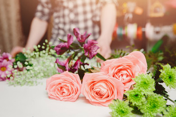 Florist man collects modern bouquet of pink roses, hibiscus.