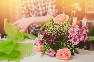 Man florist collects modern bouquet of roses, cuts scissors packaging for gift.