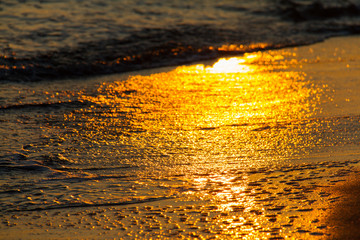 Colorful shapes of breaking waves on sandy shore at sunset