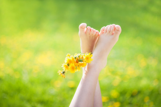 Children's legs hold a bouquet of dandelions on the background of dandelion fields in the light of the sunset sun