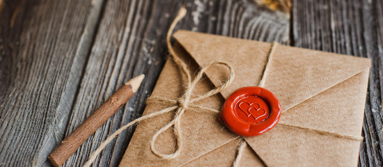 love letter in a craft envelope with a sealing wax seal in the form of a heart on a wooden background. Free space - obrazy, fototapety, plakaty