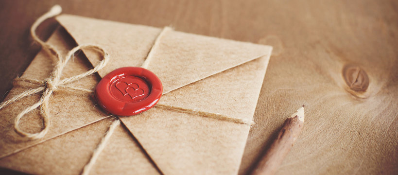 love letter in a craft envelope with a sealing wax seal in the form of a heart on a wooden background. Free space