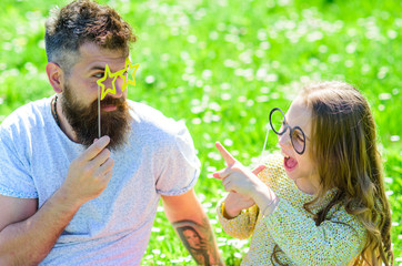 Dad and daughter sits on grass at grassplot, green background. Child and father posing with eyeglases photo booth attribute while speaking. Communication concept. Family spend leisure outdoors.