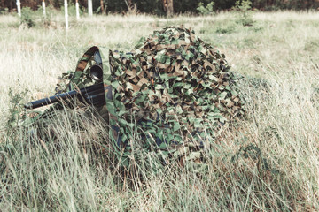 Sniper in urban combat training. Full ghillie camo suit and a high power sniper rifle. In urban combat training ground. Aiming his weapon.