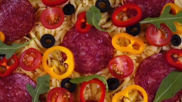 Closeup flatlay view of tasty homemade pizza with salami and vegetables rotating in 4K. Traditional tasty food.
