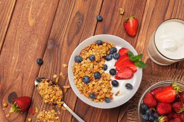 Bowl of homemade granola with yogurt and fresh berries on wooden background
