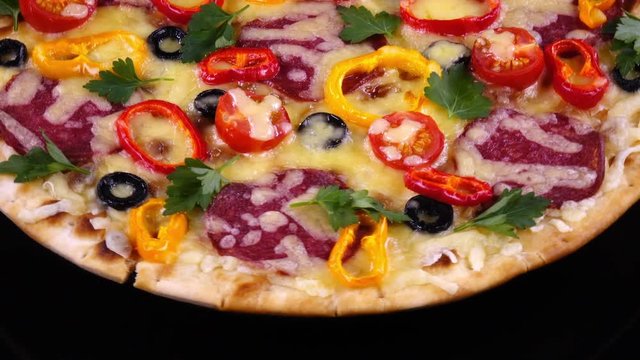 Hot homemade tasty pizza with salami and vegetables just from oven rotating on black background in 4K. Traditional tasty food.

