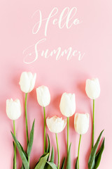 Hello summer text, white tulips on pink background. Minimal floral concept greeting card. Flat lay, top view.