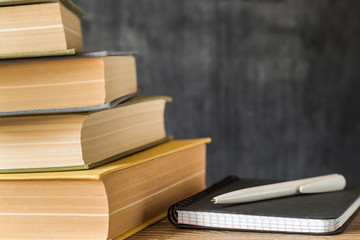 Stack of old books and notepad with pen on the wooden desk in library room. Education concept. World book day. Empty place for text on dark background.