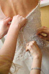 Fototapeta premium Women's hands tie a ribbon on the corset of a wedding dress. Morning gathering of the bride.