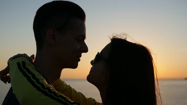 Profile of a pair in love at splendid sunset on the Black Sea shore in summer. The girl in sunglasses keeps her hands on the neck of her cutie