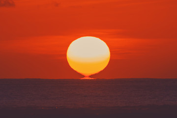 Sunrise over ocean horizon photographed with big telephoto lens.